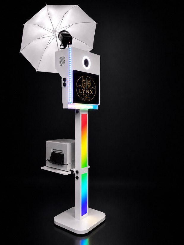 L'installation Lynxbox 39 : la borne blanche à écran tactile, surmontée
                    d'un flash de studio et de son parapluie, l'imprimante posée sur son support.