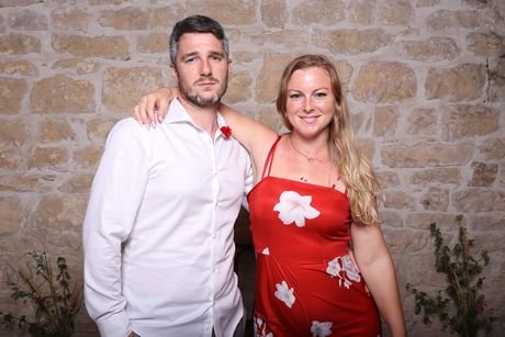 Un couple posant avec des lunettes fantaisie devant un mur de pierre.