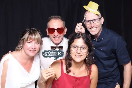 Quatre invités posant avec une pancarte « Smile » et des lunettes fantaisie.