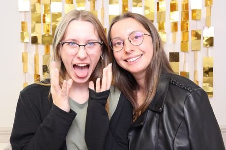 Deux invitées éclatant de rire devant un rideau de paillettes dorées.