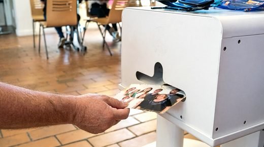 Une main retire un tirage de la fente de l'imprimante, la photo encore
                    chaude, pendant que la soirée continue à l'arrière-plan.
